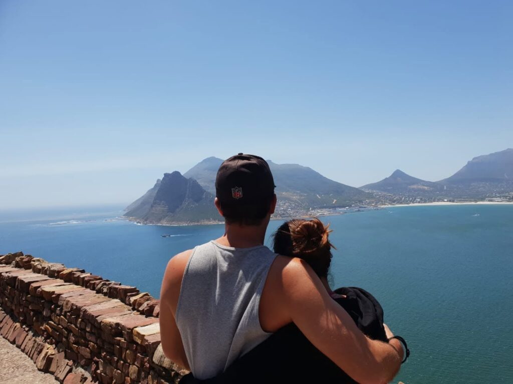A couple seen from behind, looking out at the dramatic ocean and coastal cliffs from the Cape Point viewpoint in Cape Town.